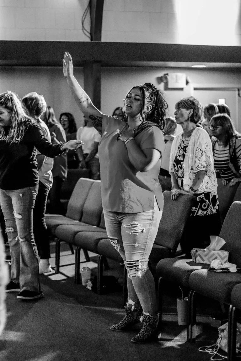 A woman with her hand over her heart and her hand raised while praying at Trinity Church Palestine, Texas.